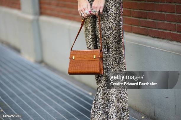 Guest wears a beige and brown leopard print pattern flowing jumpsuit, a camel shiny leather crocodile print pattern handbag, outside Fendi, during...