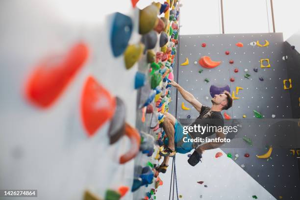 athletic man climbing indoor wall. - klimmuur stockfoto's en -beelden