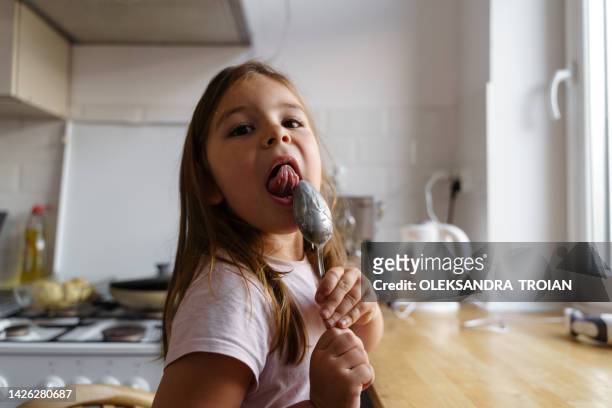 a child girl licking the spoon after baking in kitchen - girls licking girls stock pictures, royalty-free photos & images