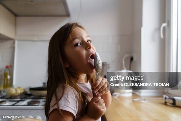 a child girl licking the spoon after baking in kitchen - girls licking girls fotografías e imágenes de stock