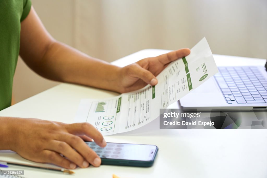 Close-up view of a woman calculating house bills with a mobile phone.