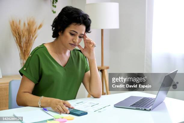 woman looking worried while calculating house bills with a mobile phone and laptop. - female worried mobile imagens e fotografias de stock