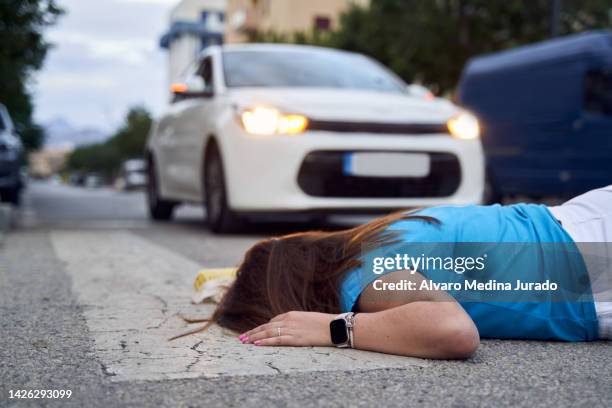 side view of an unrecognizable young woman lying on the ground at a crosswalk after being hit by a car. - accident photos death stock pictures, royalty-free photos & images