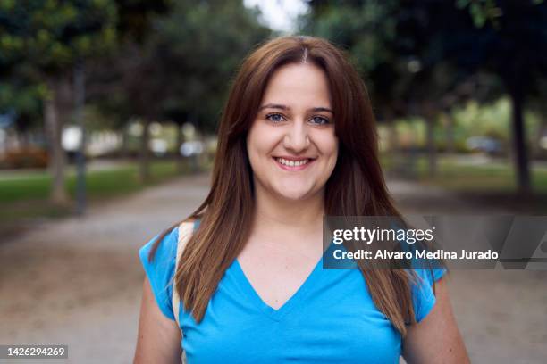 close-up frontal portrait of a happy young woman with blue eyes and dressed in blue t-shirt in a city park. - human face frontal stock pictures, royalty-free photos & images