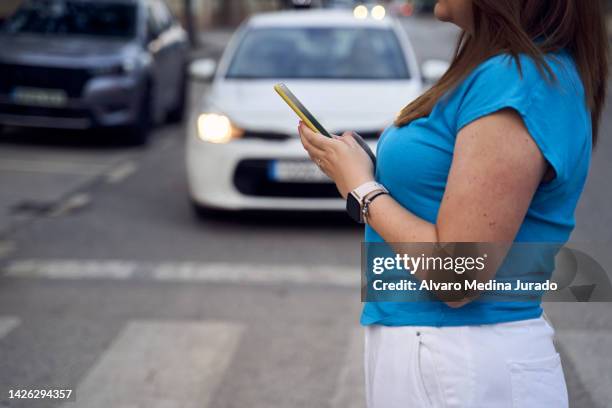 side view of an unrecognizable young woman dressed in casual clothes crossing the street at a crosswalk while distracted looking at her mobile phone. - pedestrian crash stock pictures, royalty-free photos & images