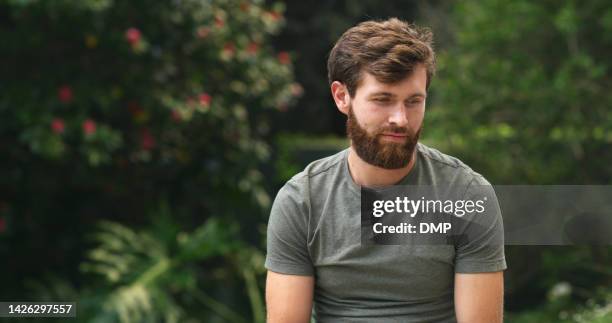 depression, sad and man thinking in nature while sitting in green garden struggling with loss or grief. thoughtful, sad and lonely guy outdoors in a park with mental health problems and broken heart. - agony in the garden stockfoto's en -beelden