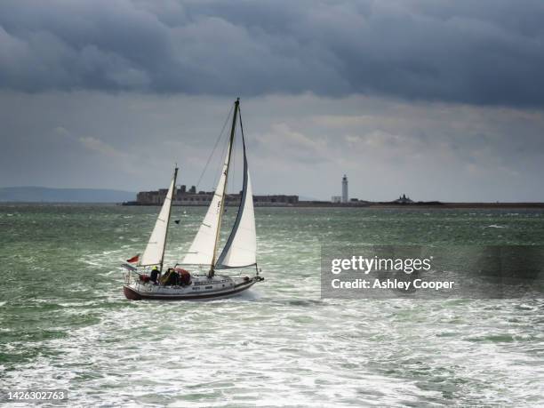 a sailboat off yarmouth on the isle of white, uk with hurst castle behind. - keyhaven photos et images de collection