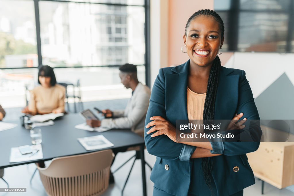 African leader, manager and CEO with a business woman in the office with her team in the background. Portrait of a female boss standing arms crossed at work during a meeting for planning and strategy