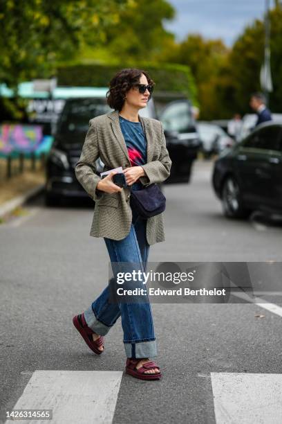 Guest wears brown sunglasses, a navy blue and red print pattern t-shirt, a beige and black checkered print pattern blazer jacket, a black suede...