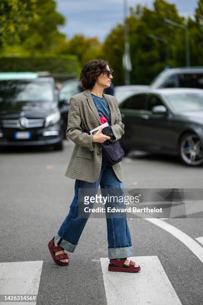 Guest wears brown sunglasses, a navy blue and red print pattern t-shirt, a beige and black checkered print pattern blazer jacket, a black suede...
