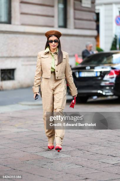 Aida Domenech wears a brown felt wool hat, black Balenciaga sunglasses, gold earrings, a green shirt, a brown denim cropped jacket, matching brown...