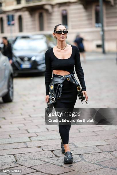 Guest wears black sunglasses, gold large earrings, a gold necklace, a black V-neck / long sleeves cropped top, a black shiny varnished leather large...