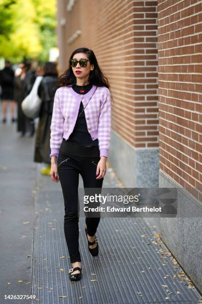 Guest wears black sunglasses, a black t-shirt, a pale purple and white checkered print pattern buttoned wool pullover, black skinny pants, black...