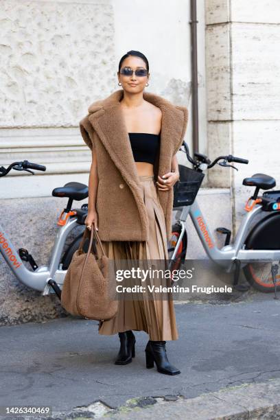 Guest is seen wearing a pleated camel skirt, a black crop top, sleeveless fur jacket and furry bag outside Max Mara show during the Milan Fashion...