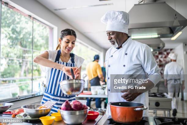 student cooking and teacher helping in a cooking class - chef demonstration stock pictures, royalty-free photos & images