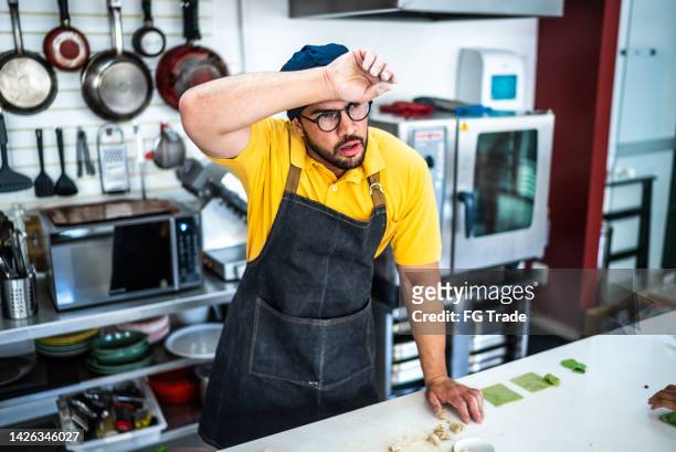 tired mid adult man making pasta in the kitchen - heat stress stock pictures, royalty-free photos & images