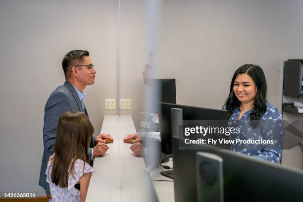 latin american man and daughter checking in at office reception desk - bank counter stock pictures, royalty-free photos & images