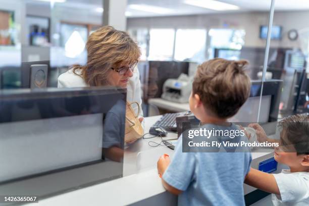 friendly receptionist greeting two young boys at office front desk - bank office clerks stock pictures, royalty-free photos & images