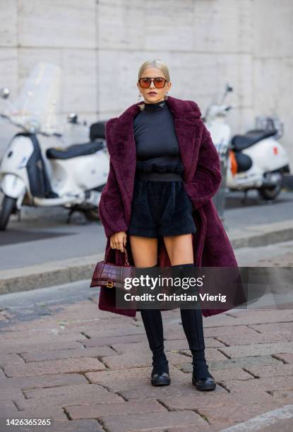 Caroline Daur wears burgundy Balenciaga bag, navy high waisted belted fleece skirt, black turtleneck, teddy coat, black over knees boots, sunglasses...