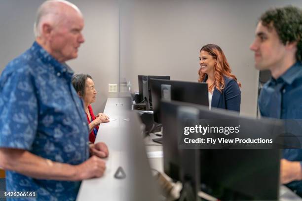 cheerful customer service representatives helping customers at reception desk - bank office clerks stock pictures, royalty-free photos & images