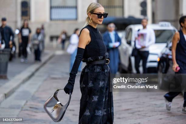 Leonie Hanne wears navy sleeveless top, high waisted belted pants, silver Gucci bag, heels, sunglasses, gloves outside Max Mara during the Milan...