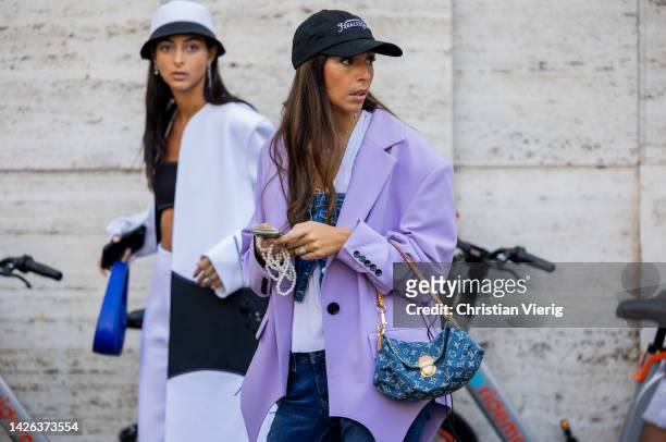 Gabriella Berdugo wears purple oversized blazer, blue Louis Vuitton bag, cap, denim jeans, cropped top outside Max Mara during the Milan Fashion Week...