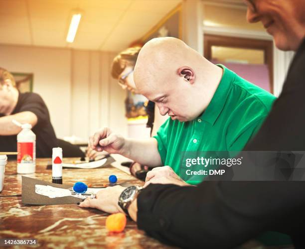 therapist helping man with down syndrome in disability support group or daycare for disabled people. teaching, special and learning for social integration, inclusion and mobility skills development - mental disability stock pictures, royalty-free photos & images