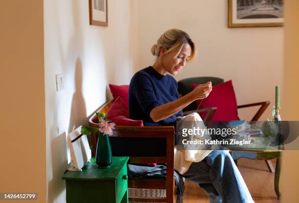 woman sitting on sofa, darning a little cashmere sweater - sewing needle bildbanksfoton och bilder