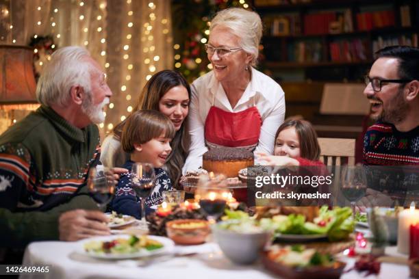 glückliche reife frau, die ihrer familie nach dem weihnachtsessen ein dessert serviert. - christmas family stock-fotos und bilder