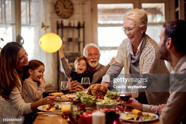 glückliche ältere frau, die ihrer familie im esszimmer eine mahlzeit serviert. - thanksgiving food stock-fotos und bilder