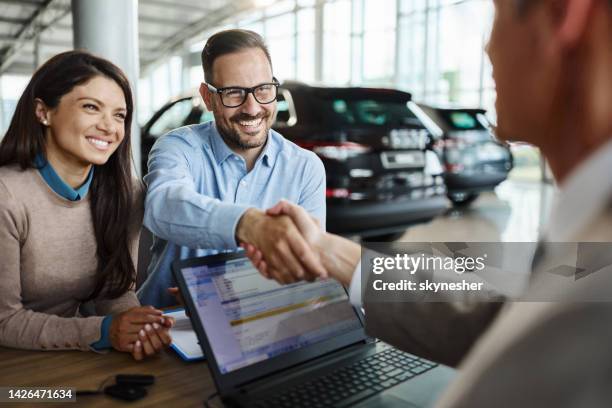 ein glückliches paar einigte sich mit einem autoverkäufer in einem ausstellungsraum. - autohändler stock-fotos und bilder