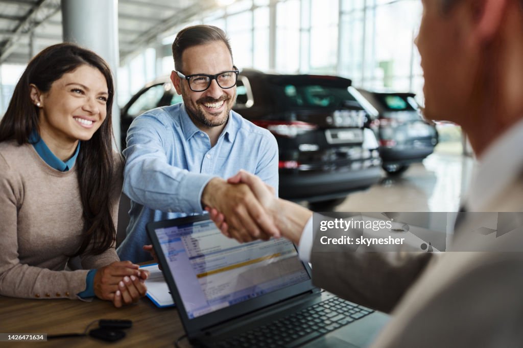 Happy couple came to an agreement with car salesperson in a showroom.