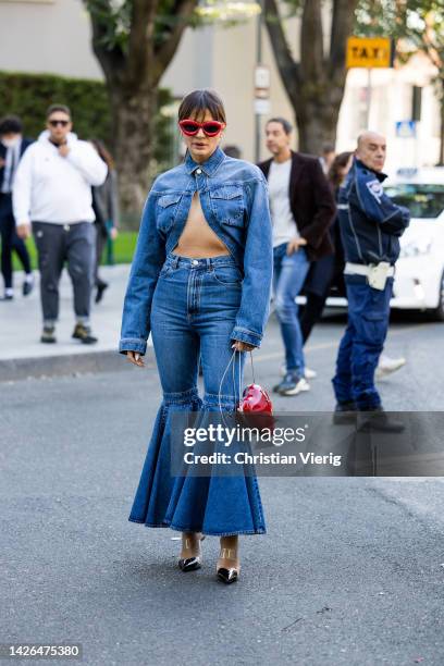 Thassia Naves wears red Loewe sunglasses, denim jacket, flared jeans, red heart shaped bag, heels outside Emporio Armani during the Milan Fashion...