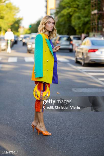 Chiara Baratello wears colorful yellow orange, blue, mint green striped blazer, skirt, bag, orange Amina Muaddi heels outside Moschino during the...