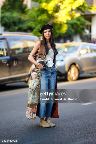 Yoyo Cao wears a black and felt with leather details beret hat, a white latte shoulder-off corset, blue faded denim straight pants, a brown with pale...