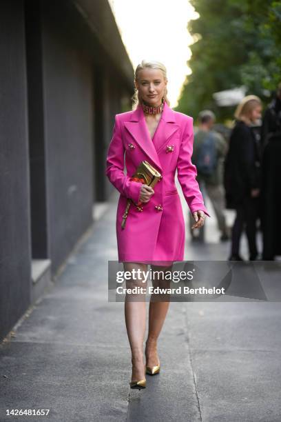 Victoria Magrath wears a gold and diamonds large logo necklace from Moschino, a pink long blazer jacket dress with embroidered large buttoned from...