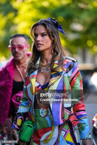 Alessandra Ambrosio wears a multicolored print pattern silk headband, a gold large chain with pendant logo pattern necklace from Moschino, a...