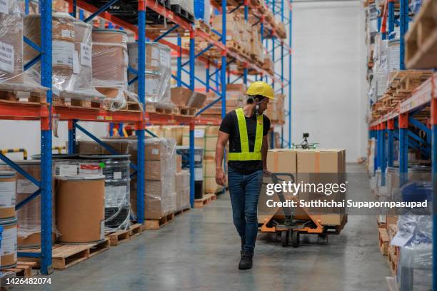 asian male worker pushing an hydraulic hand pallet truck on a warehouse. - pallet industrial equipment fotografías e imágenes de stock