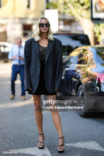 Candela Novembre wears black sunglasses, a black short dress, a black oversized blazer jacket, black strappy heels sandals , outside Armani, during...