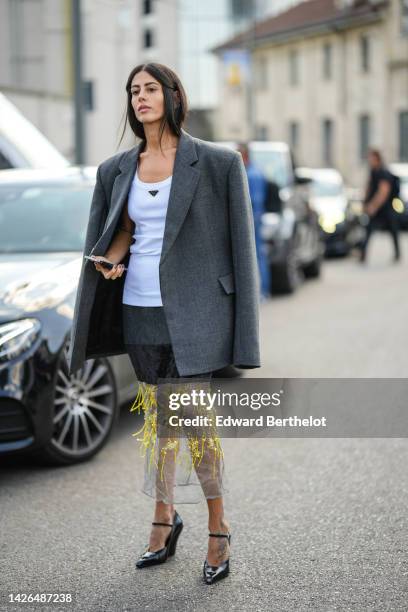 Gilda Ambrosio wears a white Prada tank-top, a gray oversized blazer jacket, half black gray with half white tulle and yellow embroidered fringed...