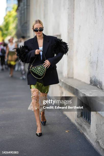 Leonie Hanne wears black sunglasses, a white tank-top from Prada, a black oversized blazer jacket with embroidered feather shoulder from Prada, a...