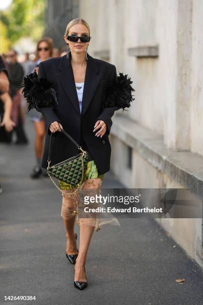 Leonie Hanne wears black sunglasses, a white tank-top from Prada, a black oversized blazer jacket with embroidered feather shoulder from Prada, a...