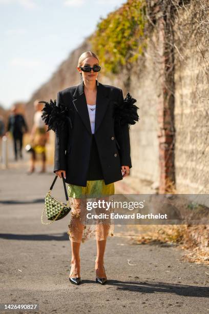 Leonie Hanne wears black sunglasses, a white tank-top from Prada, a black oversized blazer jacket with embroidered feather shoulder from Prada, a...