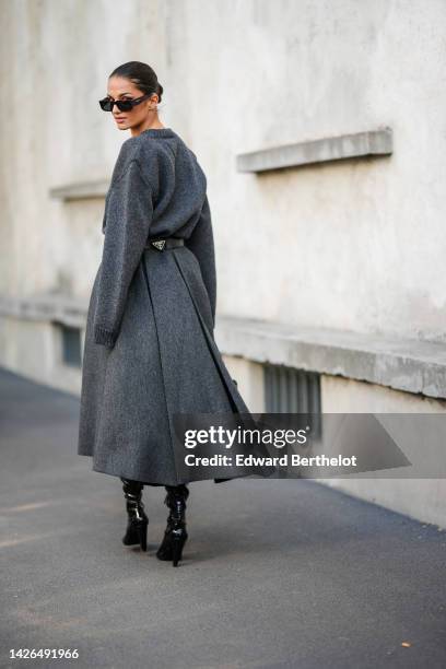 Gabrielle Caunesil wears black sunglasses from Prada, a dark gray wool long sleeves / midi long dress from Prada, a black shiny leather belt from...