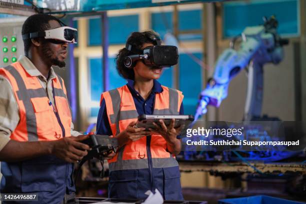 two african engineer using vr glasses for controlling the robotic welding  arm in the factory production line. - automobile industry photos et images de collection