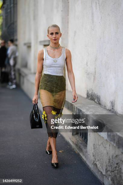 Caroline Daur wears gold and silver large necklaces, a white tank-top from Prada, a gold transparent with black tulle with embroidered yellow flower...