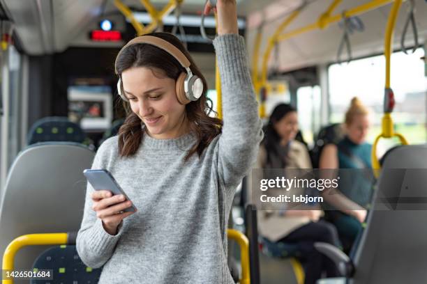 frau, die mobiltelefon und kopfhörer benutzt, während sie in einem bus musik hört - transportation hearing stock-fotos und bilder