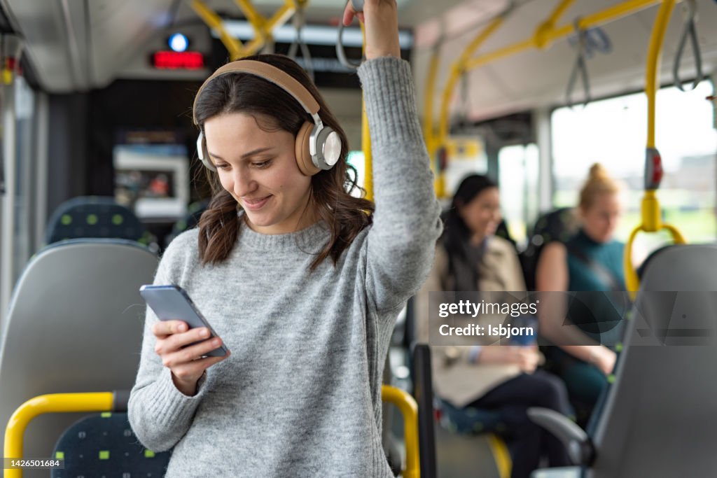 Woman using mobile phone and headphones while listening a music in a bus