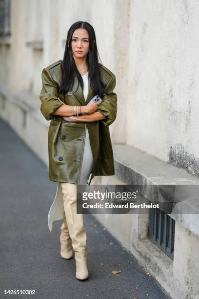 Yoyo Cao wears a khaki shiny leather oversized jacket from Prada, a white tank-top / long slit dress, beige shiny leather pointed / heels knees boots...