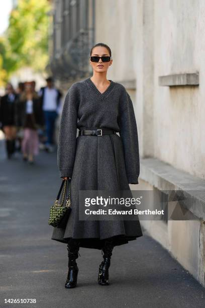 Gabrielle Caunesil wears black sunglasses from Prada, a dark gray wool long sleeves / midi long dress from Prada, a black shiny leather belt from...